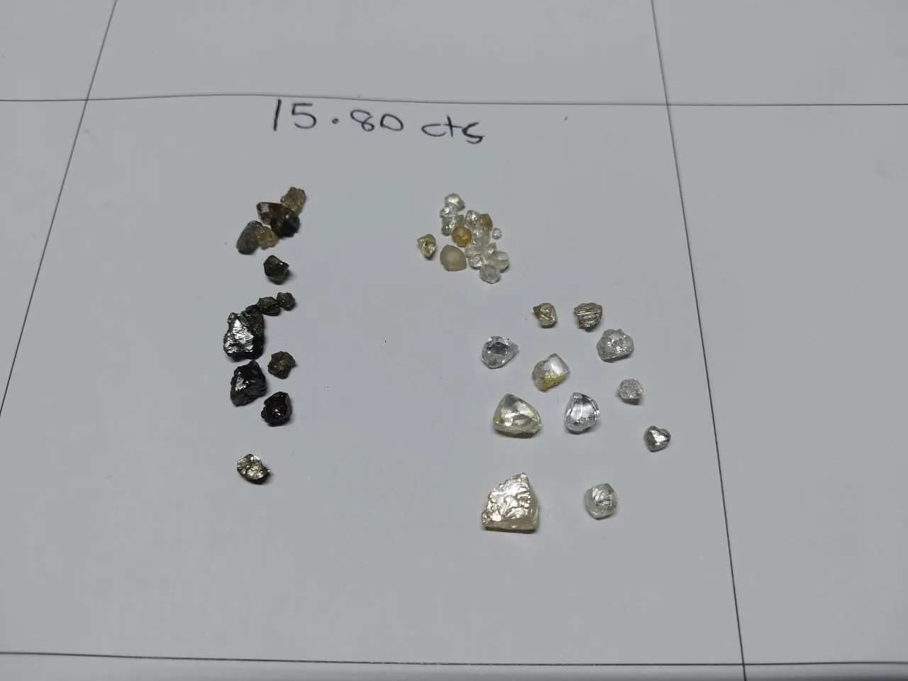 A parcel of rough diamonds laid out on paper and annotated &ldquo;15.80 cts&rdquo;, sorted into white and dark stones