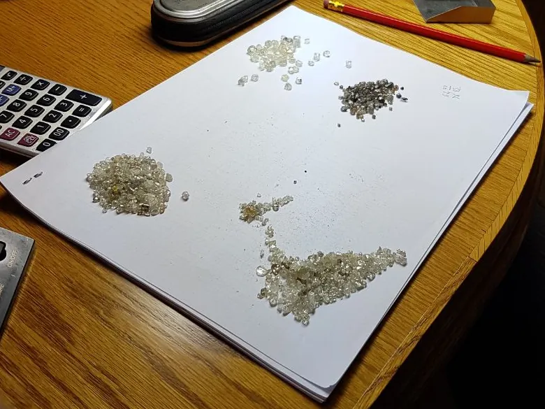 Parcels of rough diamonds laid out on paper beside a scale and loupe for sorting and weighing